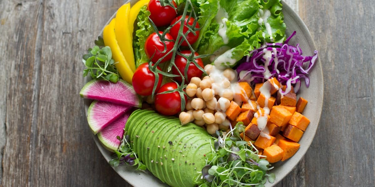 Bowl of salad with lettuce, cherry tomatoes, sliced avocado, chickpeas, purple cabbage, and roasted sweet potato