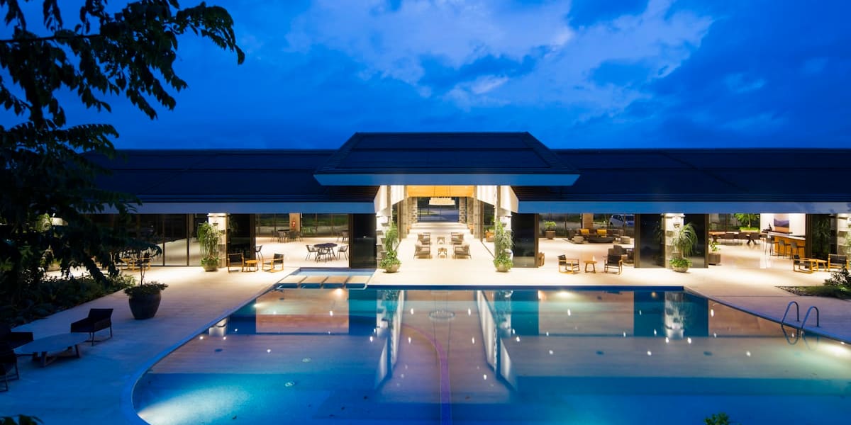 Modern resort pool and open-air lounge area lit up at dusk under a deep blue sky