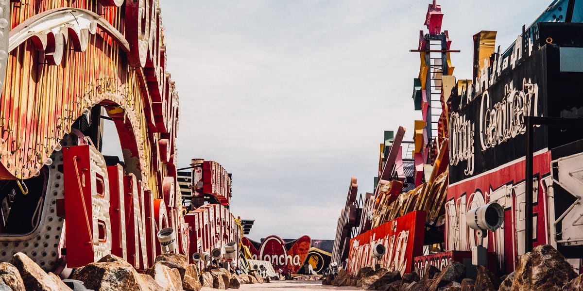 Rows of retired vintage casino and hotel signs lining a gravel path in an outdoor boneyard