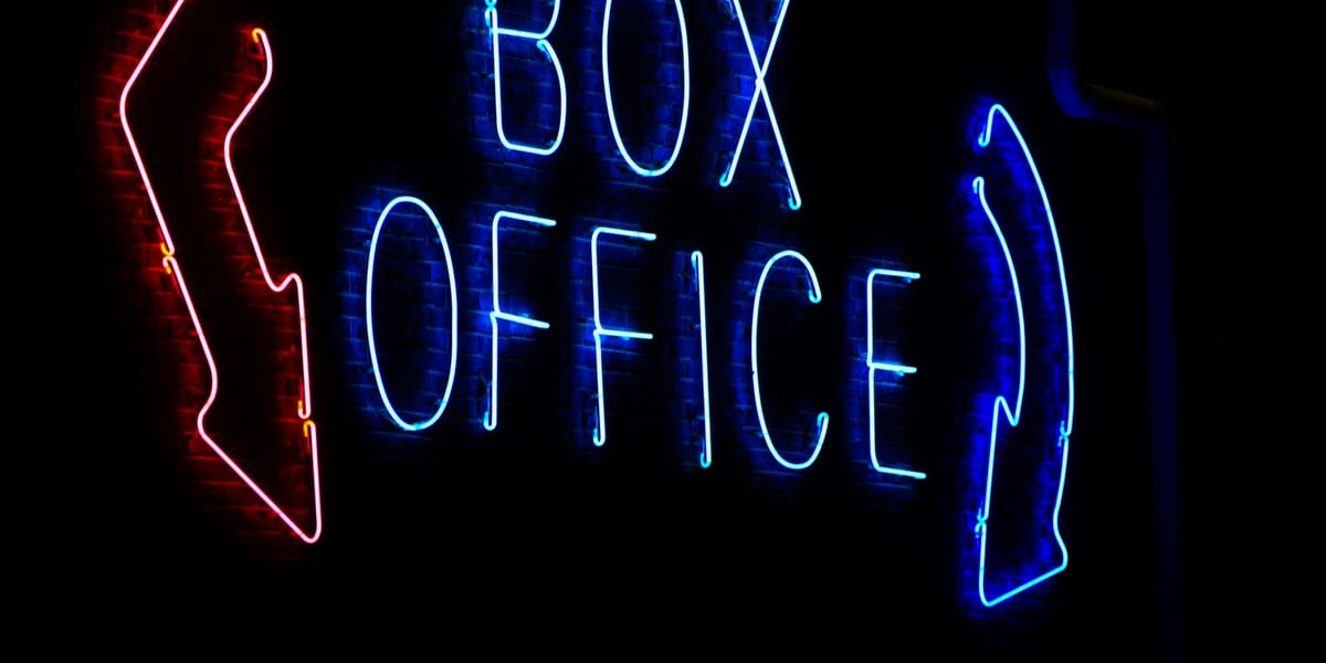 Blue neon Box Office sign with red and blue arrows glowing against a dark wall
