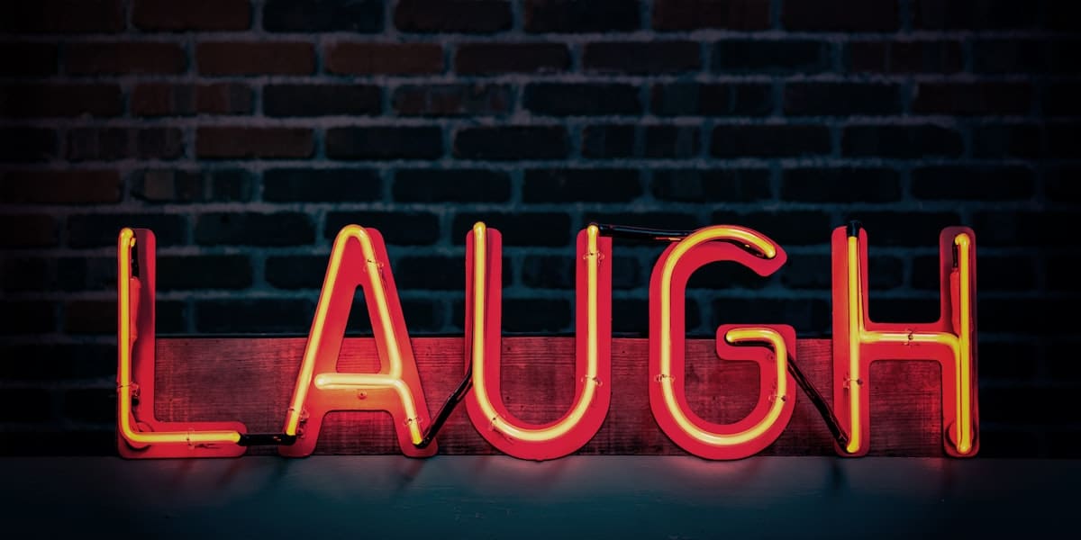 Red and yellow neon sign spelling LAUGH mounted on a dark exposed brick wall