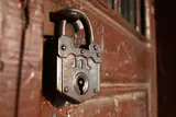 Rusty antique padlock hanging on a weathered red wooden door