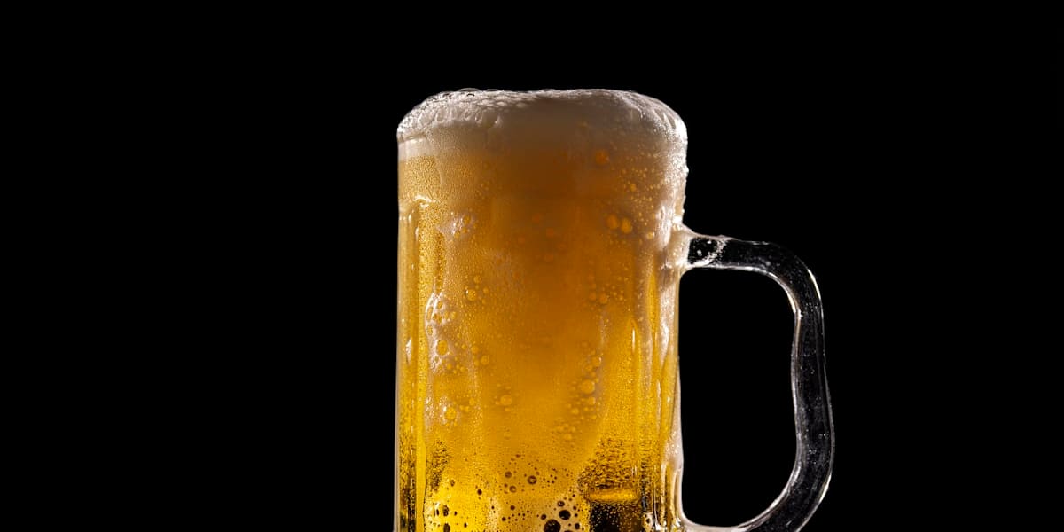 Frosty glass mug of beer overflowing with foam against a black background