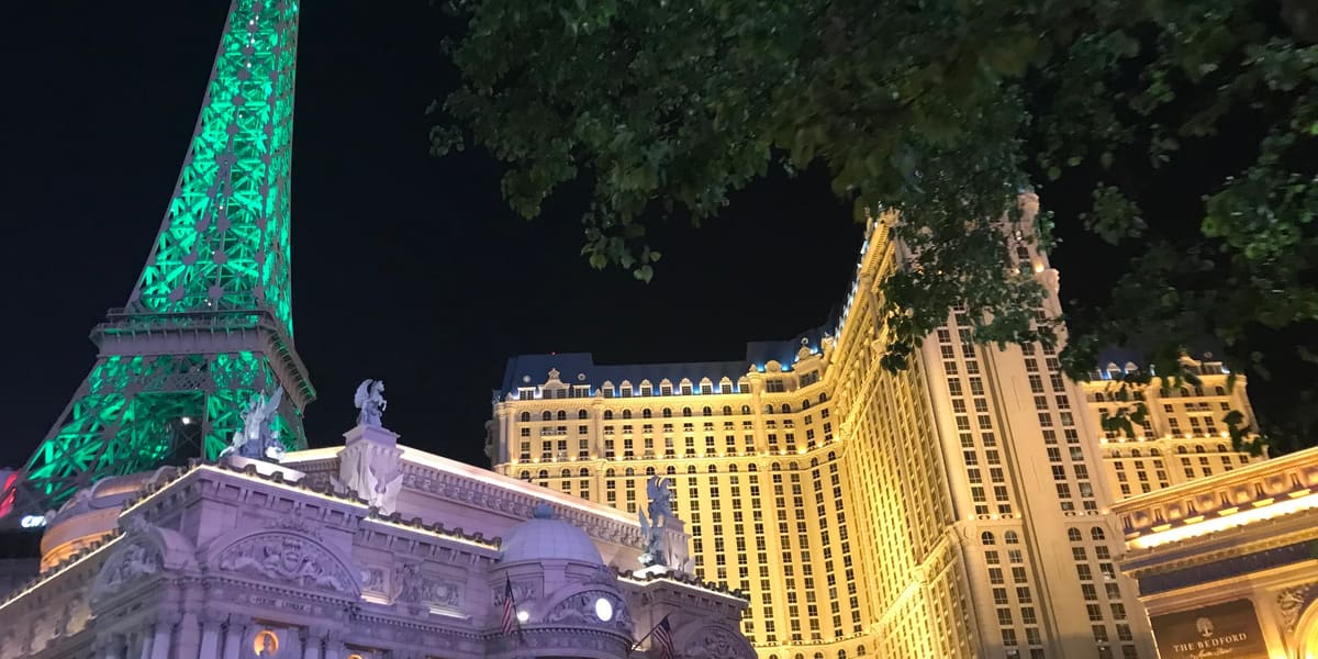 Paris Las Vegas at night, its Eiffel Tower replica lit green beside the illuminated hotel tower