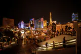 Pedestrians on escalators and sidewalks beside Las Vegas Boulevard at night, with the Paris tower lit beyond