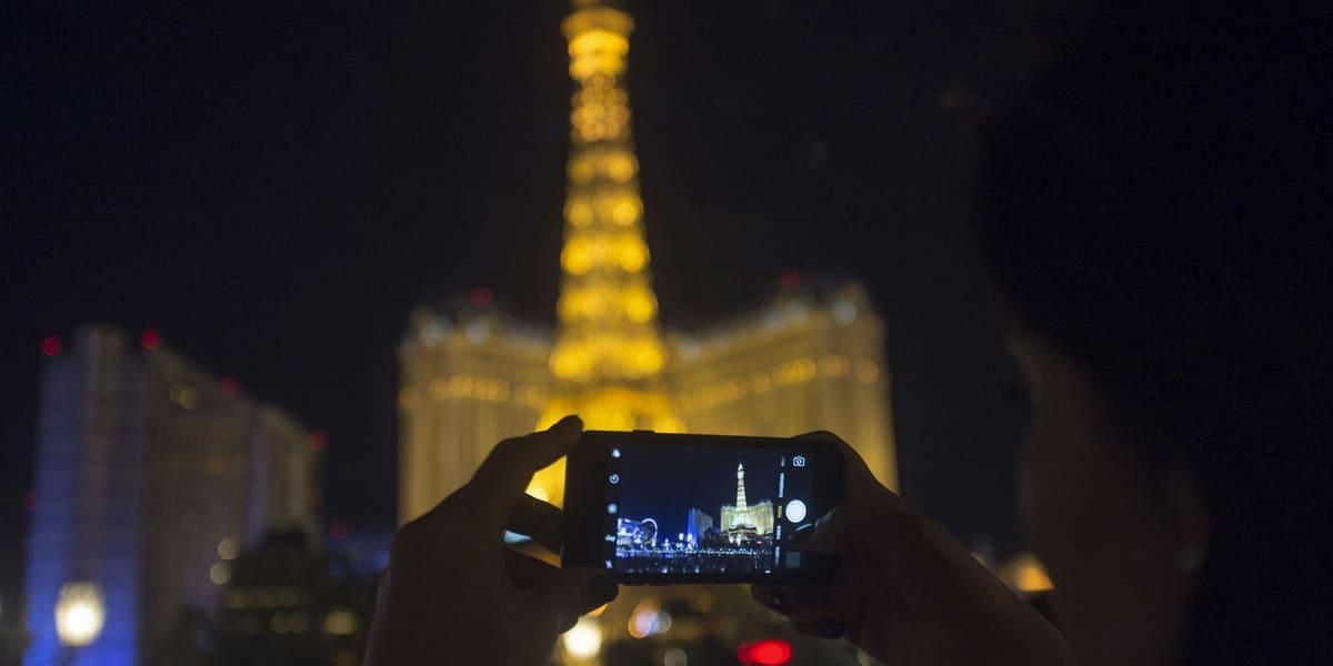 Hands holding up a smartphone to photograph a lit Eiffel Tower replica on the Las Vegas Strip at night