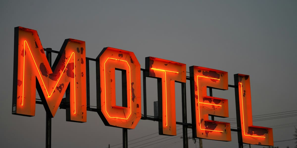 Large red neon MOTEL sign with weathered paint glowing against a grey evening sky