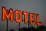 Large red neon MOTEL sign with weathered paint glowing against a grey evening sky