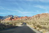 Paved road curving through desert scrub toward red and tan sandstone hills at Red Rock Canyon