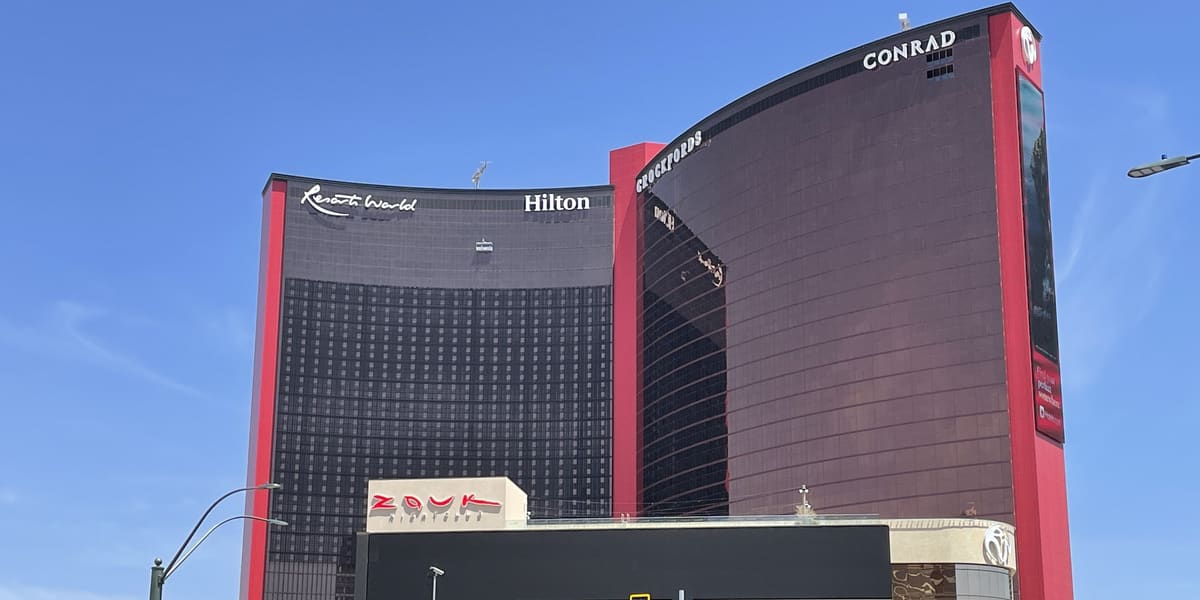 Red-framed dark glass hotel towers of Resorts World Las Vegas with Hilton and Conrad signage