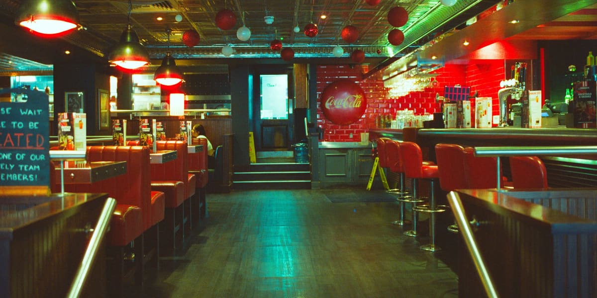 An empty retro diner with red booths, red counter stools and hanging lamps in the evening