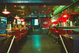 An empty retro diner with red booths, red counter stools and hanging lamps in the evening