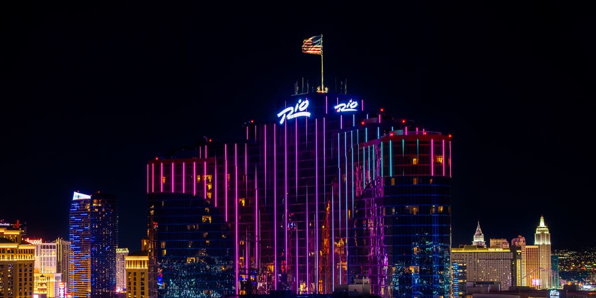 Rio hotel towers lit pink and blue at night with Rio signs and the Strip skyline behind