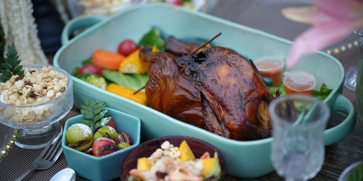 A roast turkey with vegetables in a serving dish surrounded by salads and side dishes on a festive table