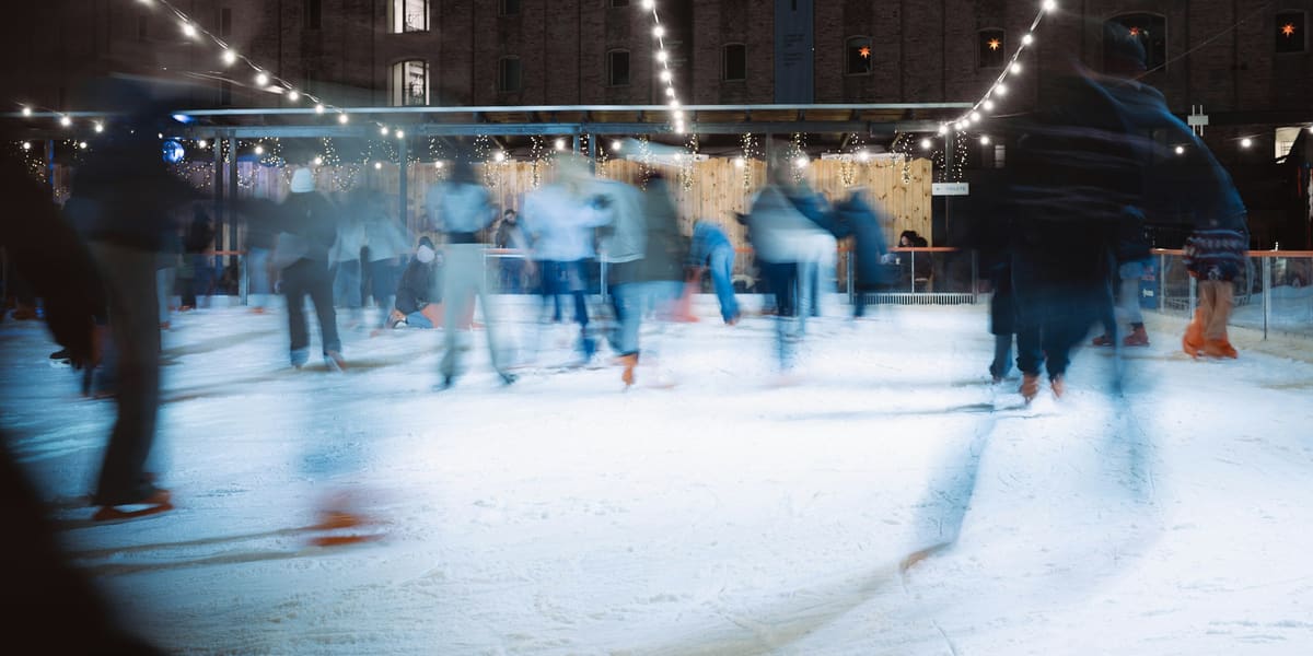 Skaters blurred in motion on an outdoor ice rink at night under strings of lights