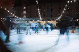 Skaters blurred in motion on an outdoor ice rink at night under strings of lights