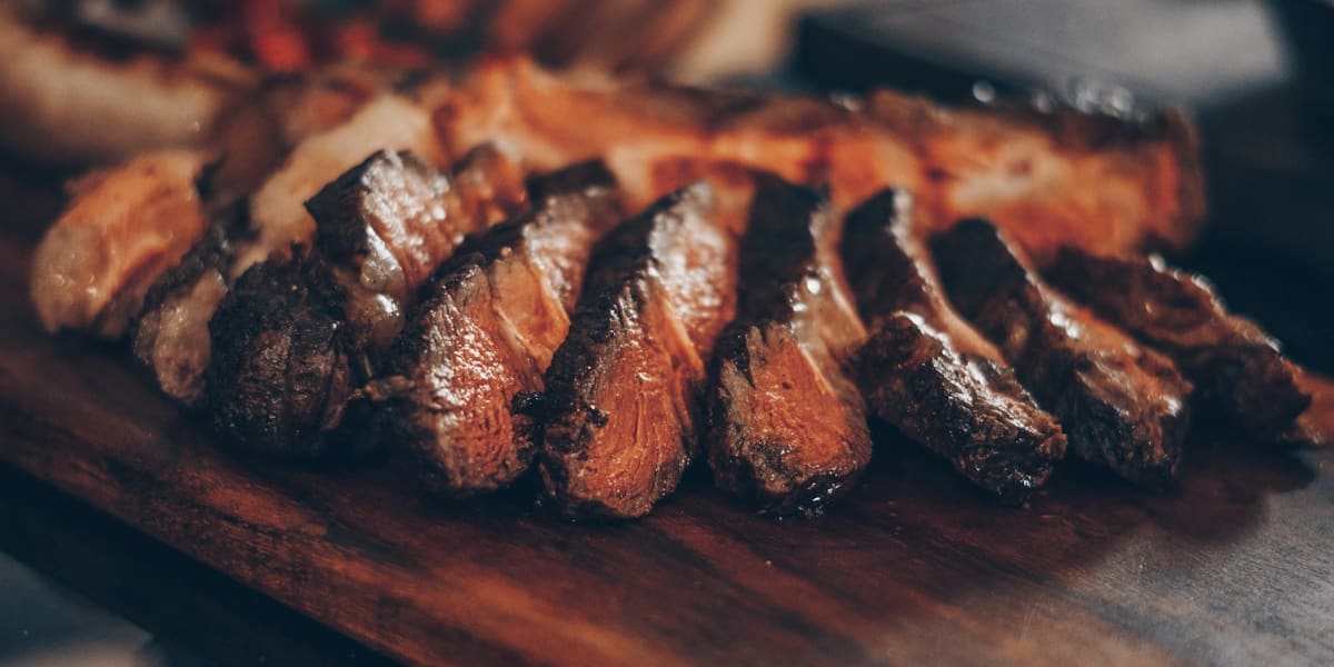 Thick slices of grilled steak with a charred crust fanned out on a dark wooden board