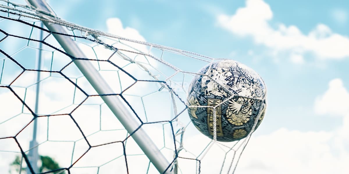 Soccer ball caught in the netting of a goal against a blue sky with scattered clouds