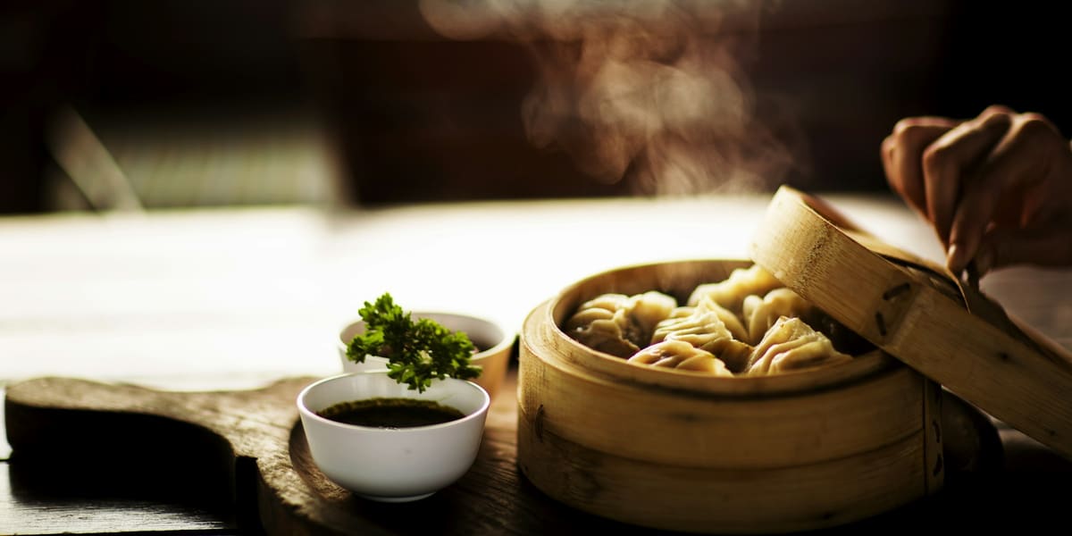 Steamed dumplings in an open bamboo steamer beside a small bowl of dipping sauce