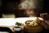 Steamed dumplings in an open bamboo steamer beside a small bowl of dipping sauce