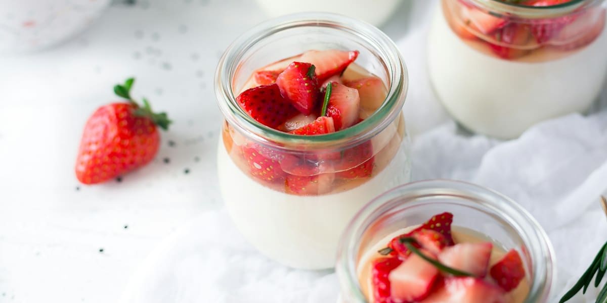 Several jars of panna cotta topped with chopped strawberries, with whole strawberries beside them