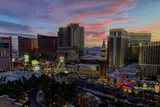 Resort hotel towers lining the Las Vegas Strip under a pink and orange sunset sky