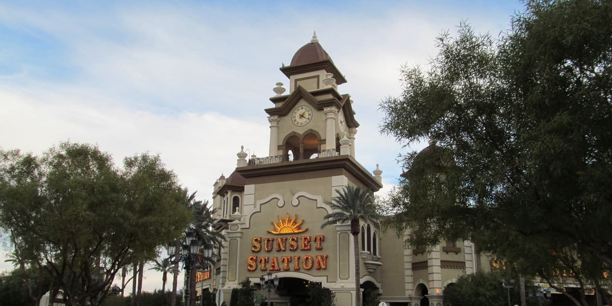 Sunset Station's clock tower entrance with its sign, framed by trees along the drive