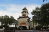 Sunset Station's clock tower entrance with its sign, framed by trees along the drive