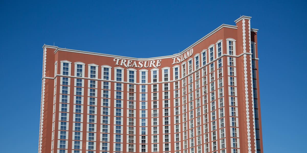 Curved red-brown Treasure Island hotel tower with its name in white letters against a clear blue sky