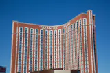 Curved red-brown Treasure Island hotel tower with its name in white letters against a clear blue sky