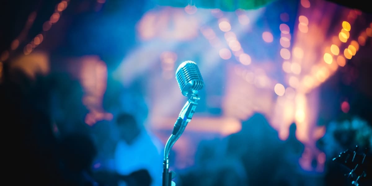 Vintage microphone on a stand silhouetted against colorful blurred stage lights and a crowd