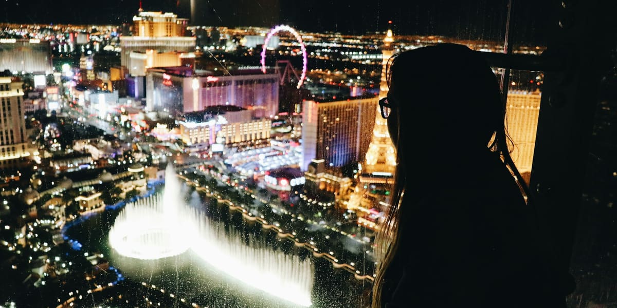 Silhouette of a woman at a window overlooking illuminated fountains, a Ferris wheel and Strip hotels at night