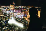 Silhouette of a woman at a window overlooking illuminated fountains, a Ferris wheel and Strip hotels at night