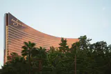 The curved bronze-glass Wynn hotel tower rising above a line of green trees