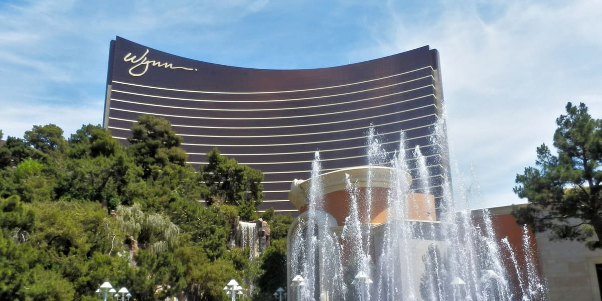 The curved bronze Wynn Las Vegas tower behind trees, a pond and a spraying fountain