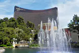 The curved bronze Wynn Las Vegas tower behind trees, a pond and a spraying fountain